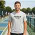 Man wearing a 'Pickleball Est. 1965' t-shirt on a tennis court.